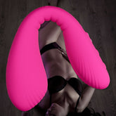 A person wearing black lingerie lounges on a dark wooden floor, with a large pink inflatable object arched over their body, and a Lovense Dolce G-Spot and Clitoral Stimulator by their side.